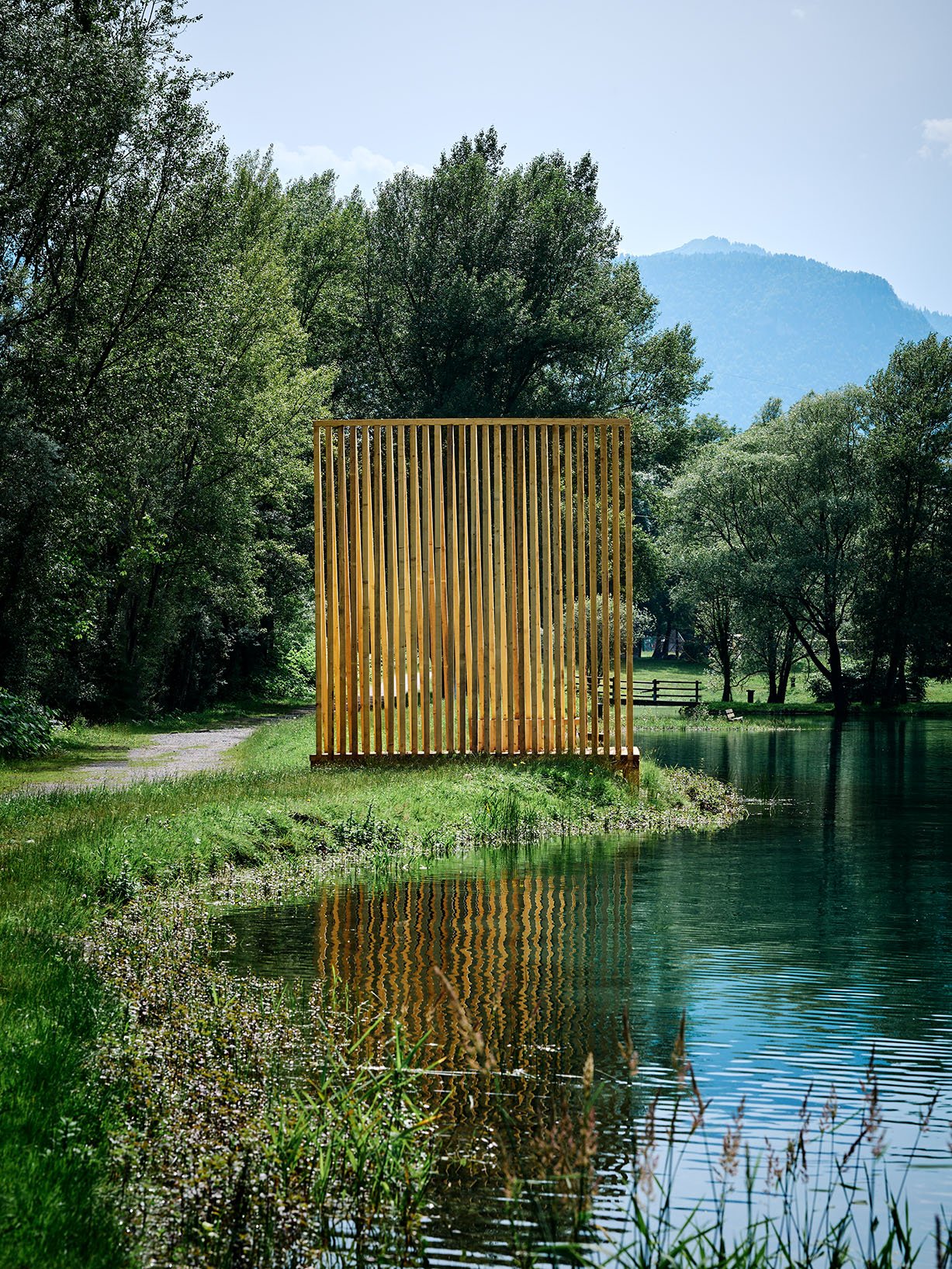 Rear view of a timber lattice pavilion positioned at the edge of a mountain lake.