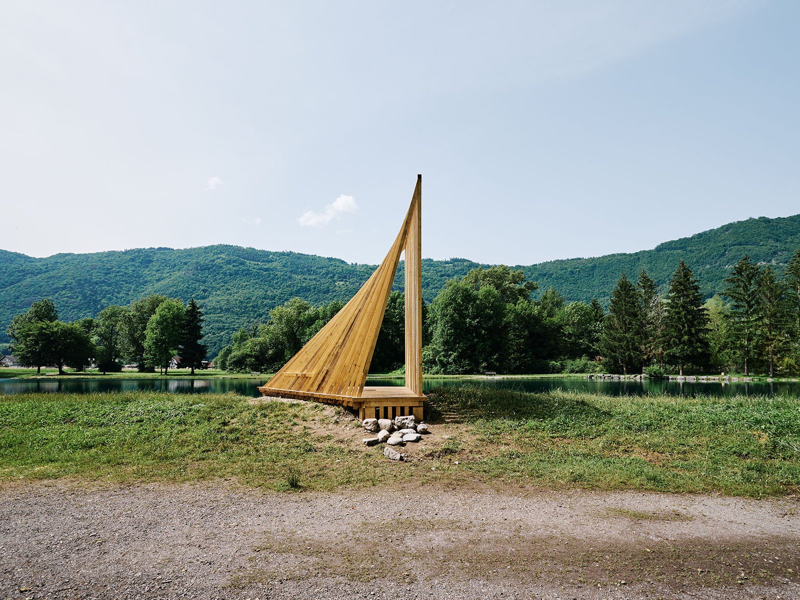 Sail-inspired timber installation overlooking a lake, defined by elegant lines and an open structure.