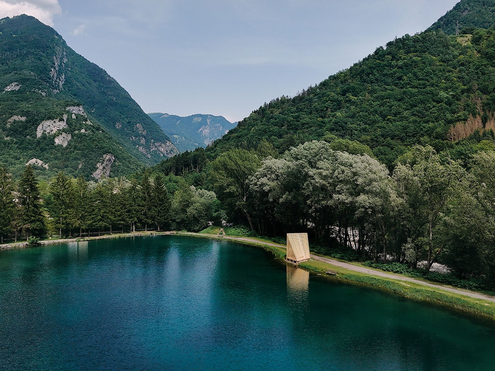 Aerial view of a timber pavilion set along a mountain lake, surrounded by forest and alpine scenery.
